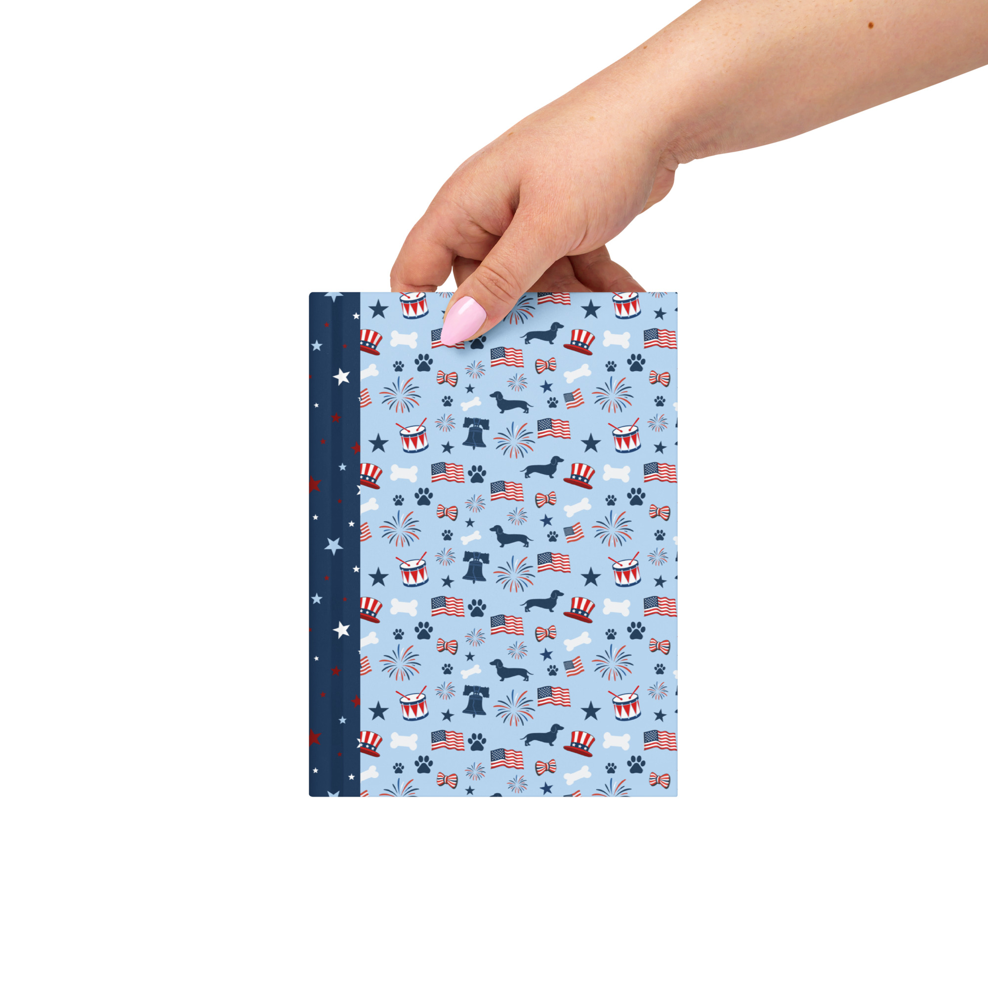 Front cover of the white matte hardcover journal, positioned to show the flexible, sewn navy blue spine adorned with red and white stars and a central celebratory dachshund illustration.