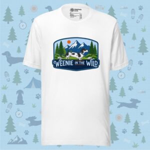 Front layout view of a solid white unisex crewneck t-shirt displayed flat. The shirt features the large, colorful "Weenie in the Wild" adventure graphic patch centered on the chest, surrounded by a decorative light blue background pattern.